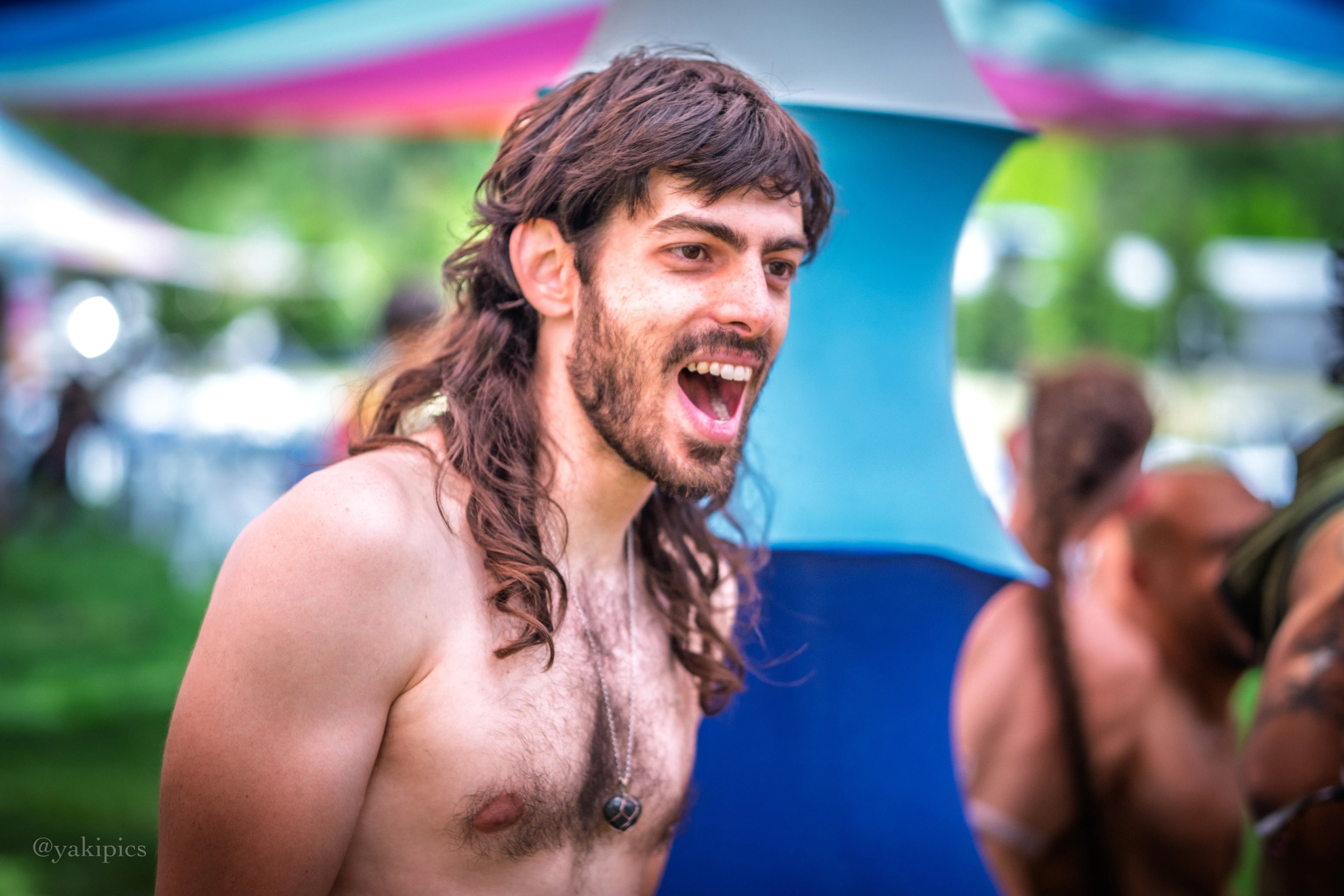 Yoav laughing mid-conversation at a festival, under a colorful striped canopy